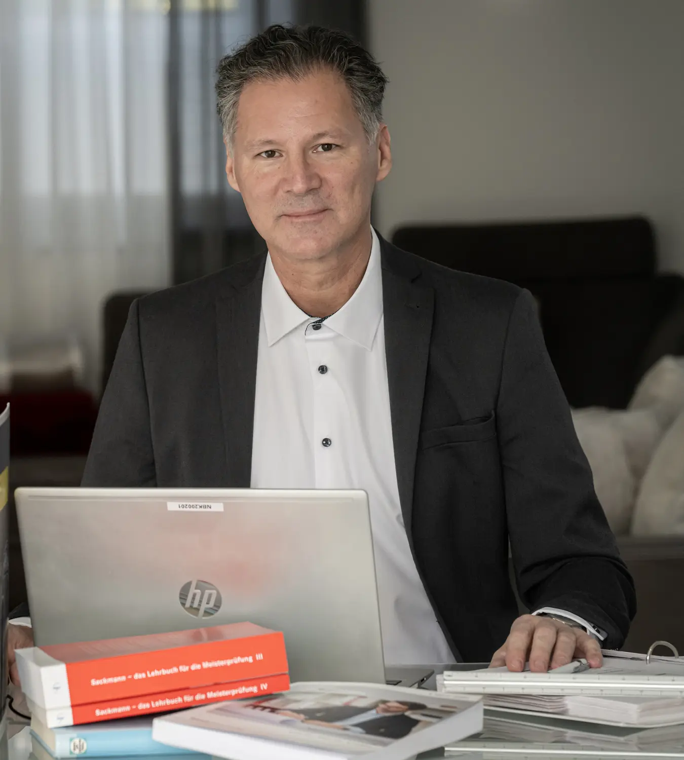 Auf diesem Bild sehen Sie einen Mann im Anzug an seinem Arbeitsplatz vor seinem Laptop sitzend