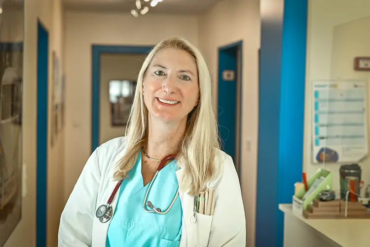 Auf diesem Bild sehen Sie eine blonde Krankenschwester, die in einer Praxis in die Kamera lächelt