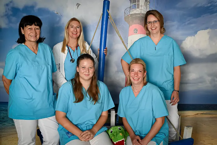 Auf diesem Bild sehen Sie das gesamte Team einer Praxis vor einem maritimen Hintergrund