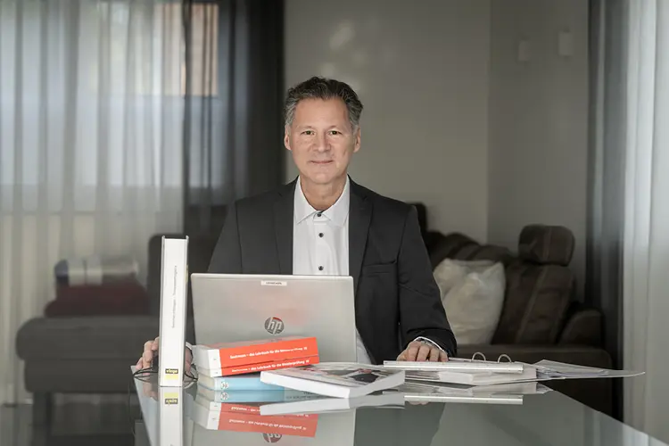 Auf diesem Bild sehen Sie einen Mann im Anzug an seinem Arbeitsplatz vor seinem Laptop sitzend