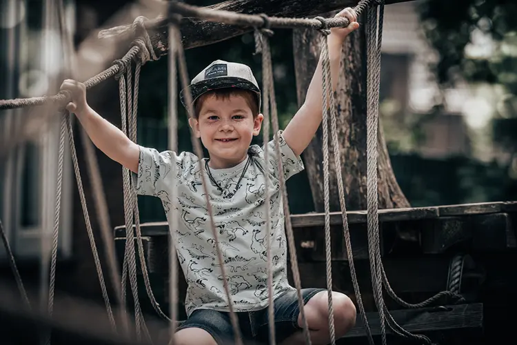 Auf diesem Bild sehen Sie einen kleinen Jungen , der sich in einem Klettergerüst auf dem Spielplatz in den Seilen festhält