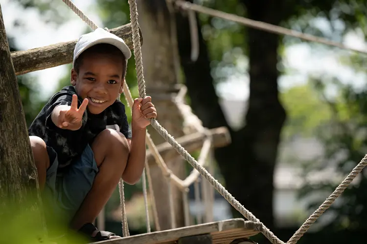 Auf diesem Bild sehen Sie einen kleinen Jungen , der sich in einem Klettergerüst auf dem Spielplatz in den Seilen festhält