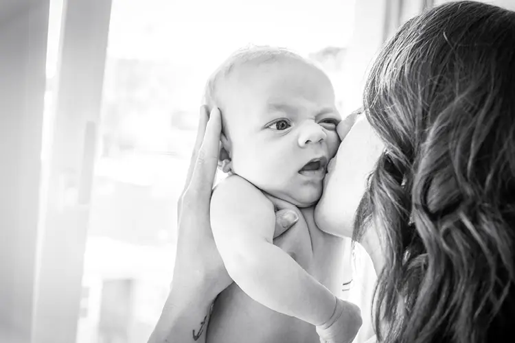 Auf diesem Bild sehen Sie ein kleines Baby, was liebevoll von seiner Mama in den Arm genommen und dabei geküsst wird