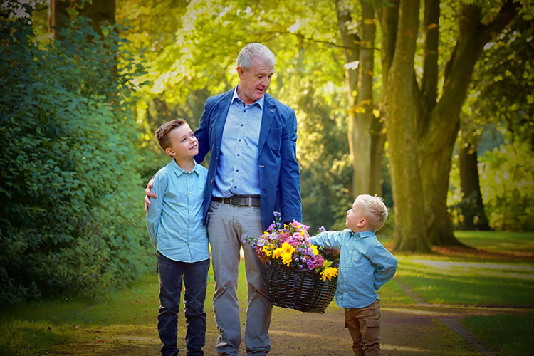 Auf diesem Bild sehen Sie einen Opa mit seinen beiden Enkeln, der einen Korb mit Blumen in der Hand hält