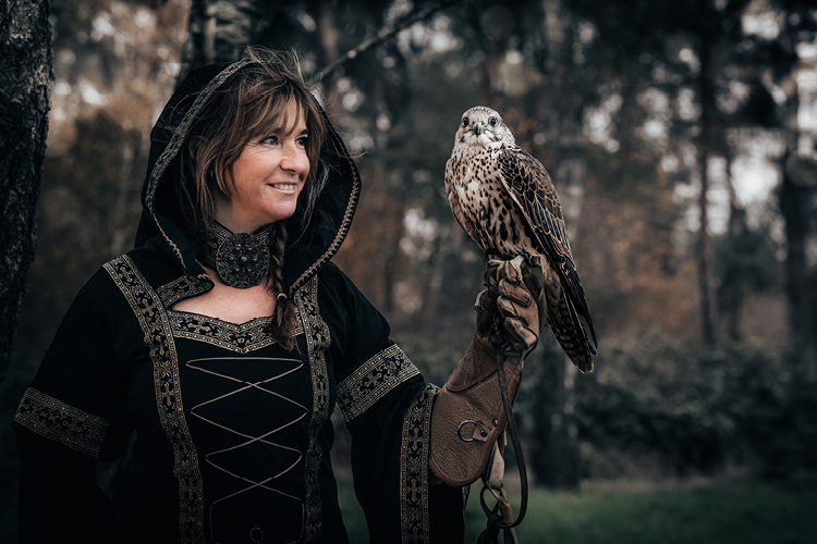 Auf diesem Bild sehen Sie eine Frau in mittelalterlicher Tracht, die einen Greifvogel auf der Hand sitzen hat