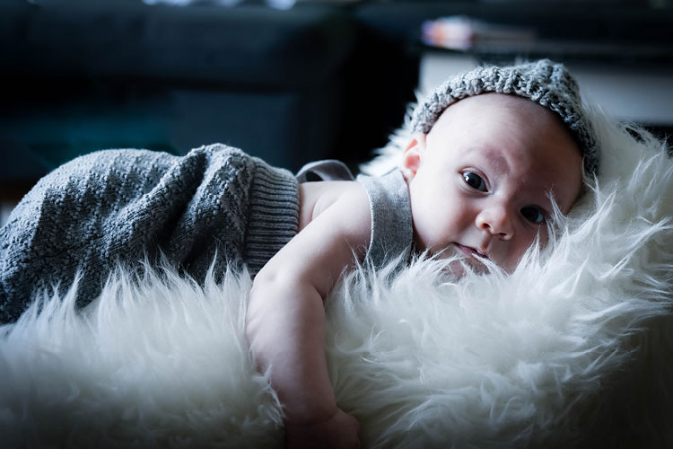Auf diesem Bild sehen Sie ein neu geborenes Baby mit geöffneten Augen auf einem weichen Fell liegend