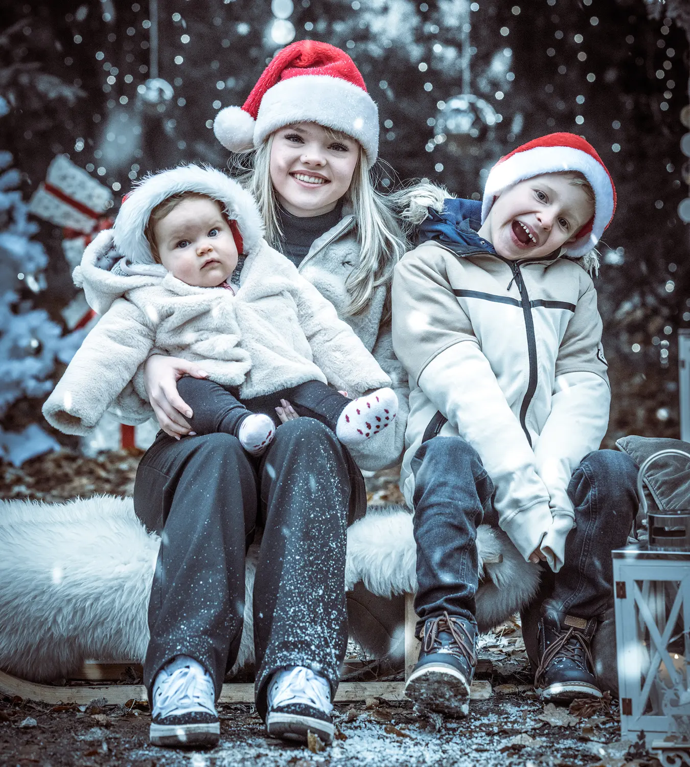 Auf diesem Bild sehen Sie eine Familie, die frohlich in weihnachtslicher Stimmung umgeben von Geschenken, Tannenbäumen und Kugeln mit Weihnachtsmützen in die Kamera lächelt