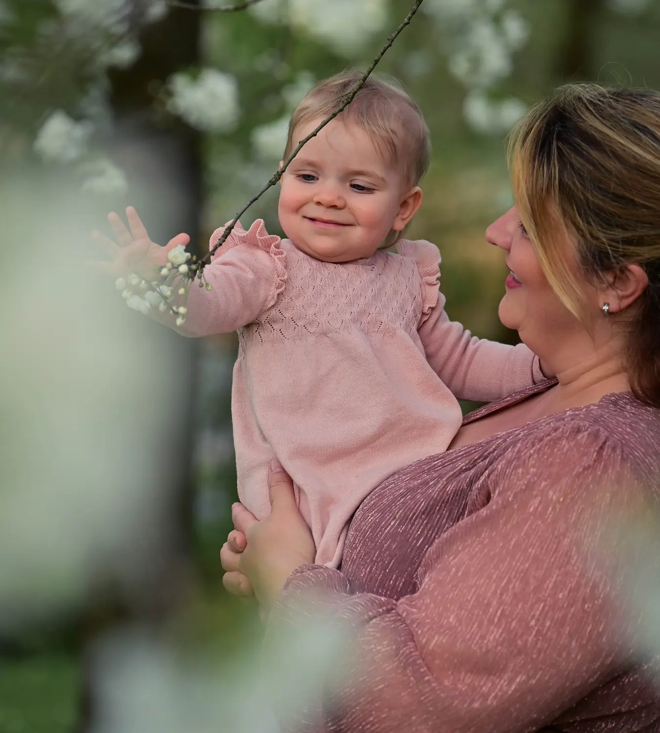 Auf diesem Bild sehen Sie eine Frau mit ihrem Baby auf den Arm, was gerade nach den Kirschblüten im Baum greift